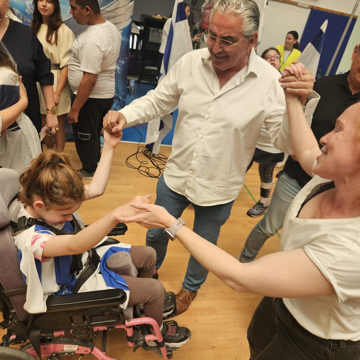 ילדה בכיסא גלגלים רוקדת יד ביד עם מבוגרים במעגל בכנס