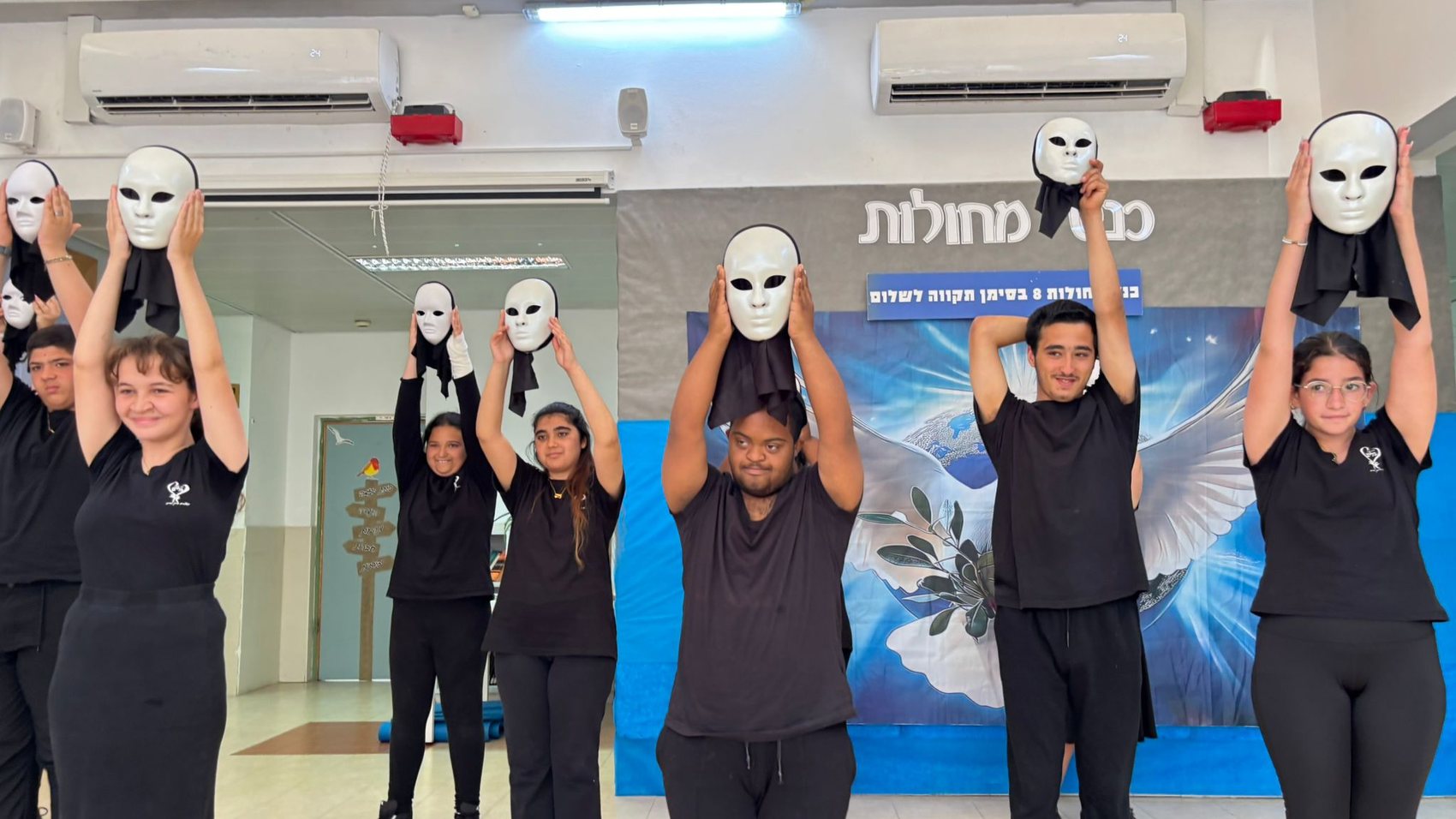 קבוצת תלמידים לבושים בשחור מרימים מסכות לבנות במופע בנושא תקווה לשלום
